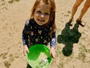 A little girl holding a fish in a bucket at a youth fishing tournament.
