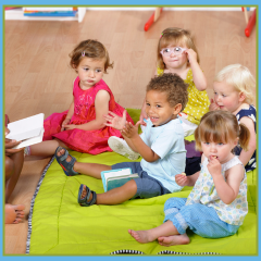Young children sitting on mat looking at someone reading a book