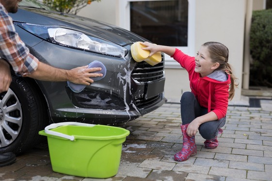 Young girl in red jacket helps parents was a black car with sponge