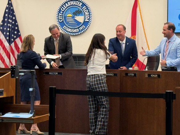 Two staff shaking hands with three City Council members behind the Clearwater City Council dais 