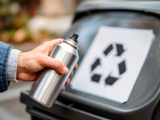 Person holding spray can in front of recycling