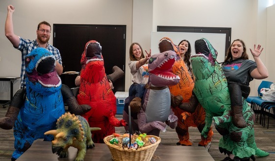 Image of librarians wearing dinosaur costumes, jumping in the air in celebration of the 2026 Summer Reading Program