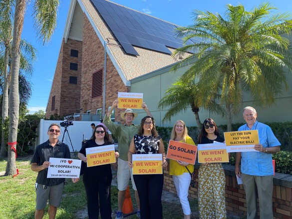 Group of people holding signs in front of church with solar panels