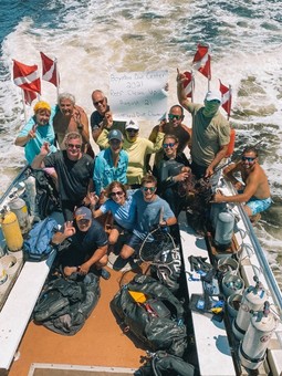 A group of divers pose on the back of the boat with a “2021 Reef Clean Up” sign.