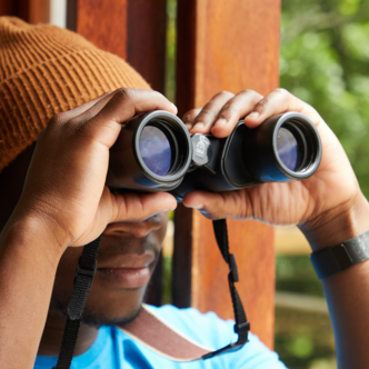 A man in an orange beanie looks through a pair of binoculars