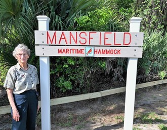 Phyllis Mansfield stands next to a sign declaring the site's new name