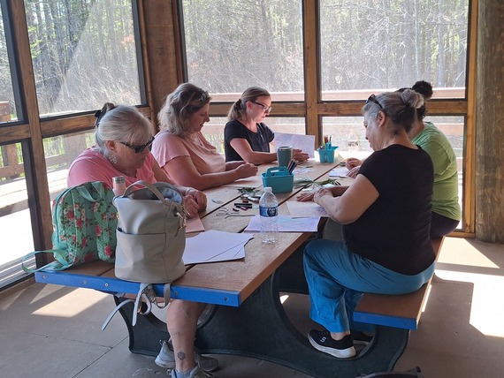 Five women drawing pictures at a picnic table.