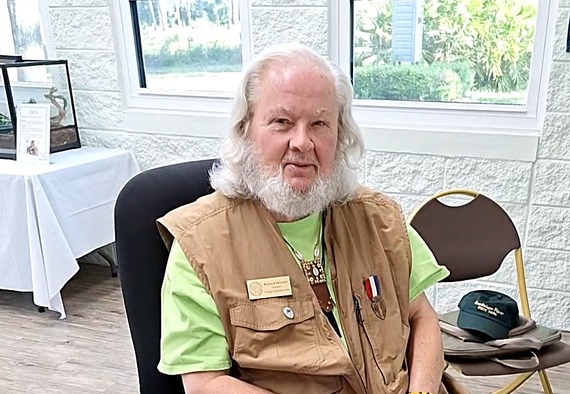 A mature white man sitting in a chair, looking at the camera, inside a nature center.