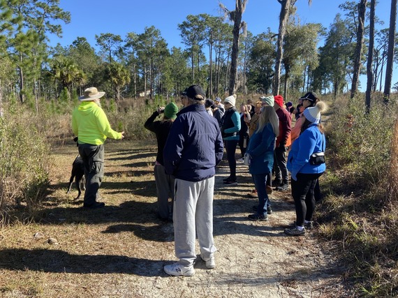 a man in a neon green sweatshirt speaking to a group of adults on a hiking trail outdoors