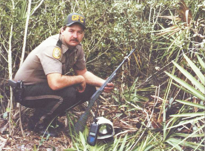 officer kneeling in brush holding gun