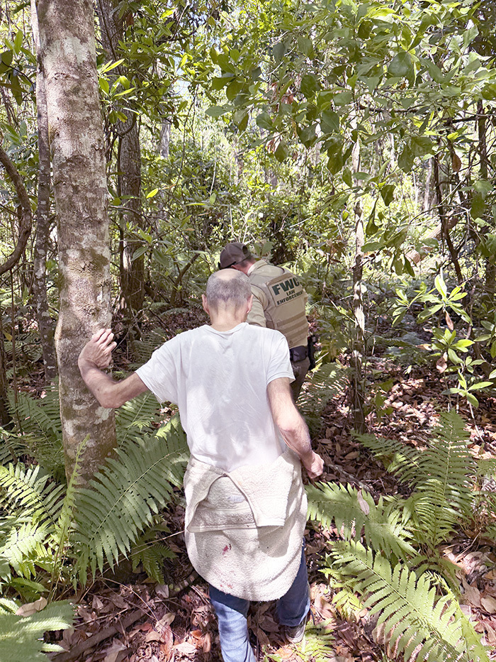 thin man following FWC officer through thick forest