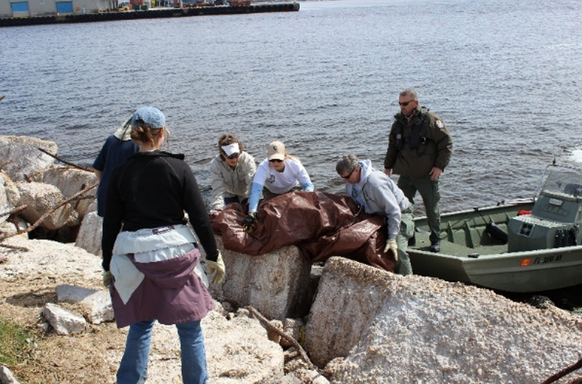 FSA partners moving a large tarp cover from a boat onto a rocky shore