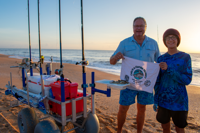 Adult and child with Catch a Florida Memory towel and fishing gear on beach