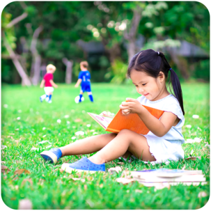 Girl reading, boys playing soccer nearby