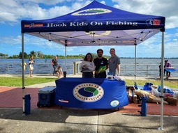 three people posing under a tent called Hook Kids on Fishing