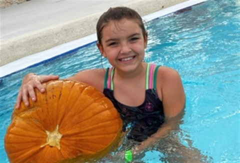 Little girl in pool smiling with pumpkin