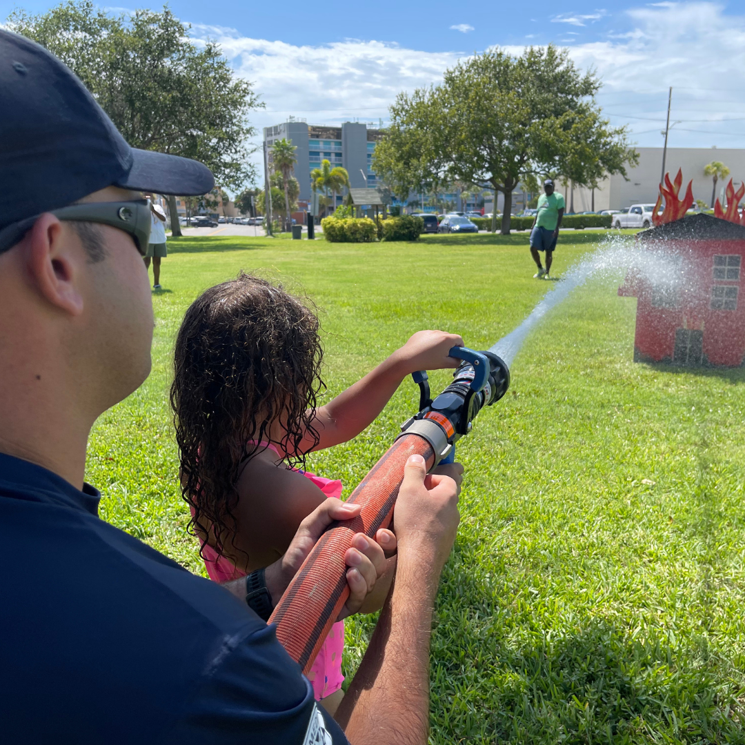 Treasure Island Fire Rescue Summer Camp Splash Down. Firefighter helping girl spray hose.