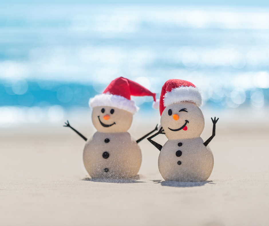 Two sand snowman on a beach with Santa hats on