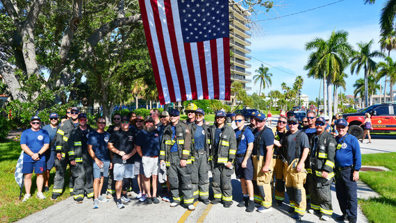 Group of area firefighters together under a large American flag after 9-11 Memorial Walk