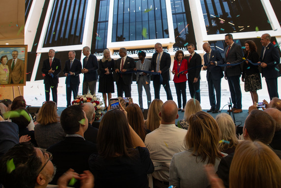 Mayor James and others stand on stage cutting a ribbon with confetti in the air 