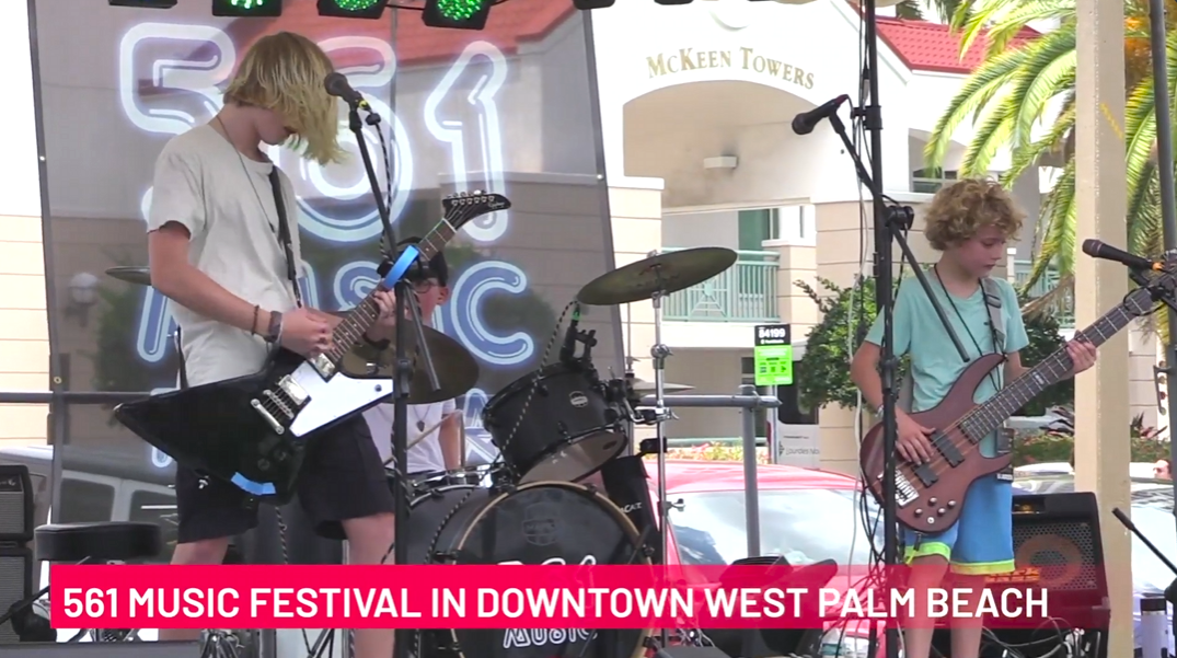 Two blond-haired kids play guitars on a stage and there's text that says "561 Music Festival in Downtown West Palm Beach"