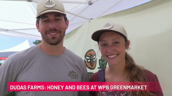 Man and woman smile at camera wearing baseball caps. These words are shown - Dudas Farms, Honey & Bees at WPB GreenMarket