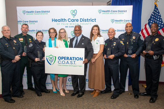group of people, including uniformed personnel, stand together holding an "Operation C.O.A.S.T." sign.