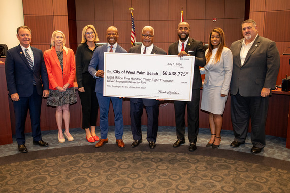 Group of people holding a giant check in West Palm Beach City Commission Chambers. Mayor and Commissioners make up the group. 