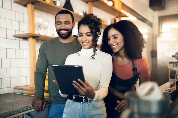 three people looking at tablet, smiling, in what appears to be a work environment