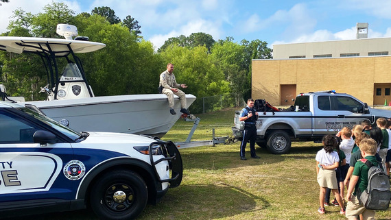 Police and Marine Patrol officers with their boat, car and truck visiting kids at school