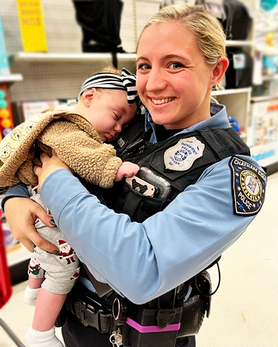 image of smiling female police officer holding a sleeping baby in a store