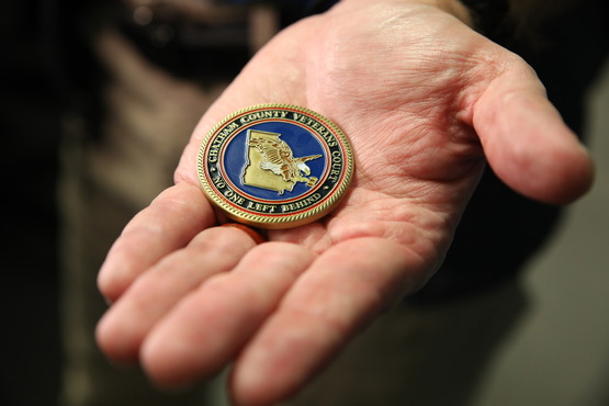 image of man's hand holding military challenge coin reading "no one left behind"