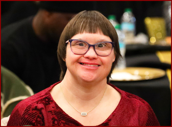 young woman with downs syndrome smiles broadly as lights from the Therapeutic Holiday Ball are reflected in her eyes