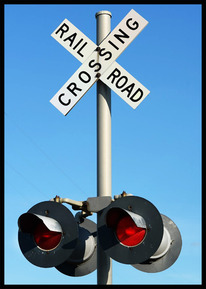 Railroad crossing sign and flashing lights against blue sky