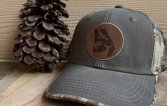 Gray/brown DNR cap beside brown longleaf pine cone against brown/gray background