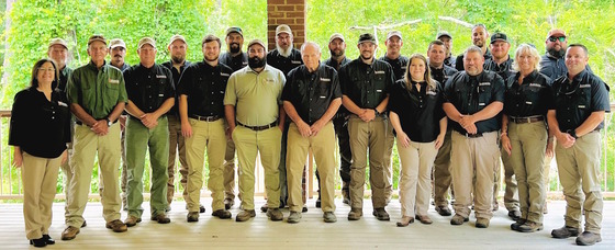 Row of DNR staff, most in black shirts, khaki pants, against brown and bright green backdrop