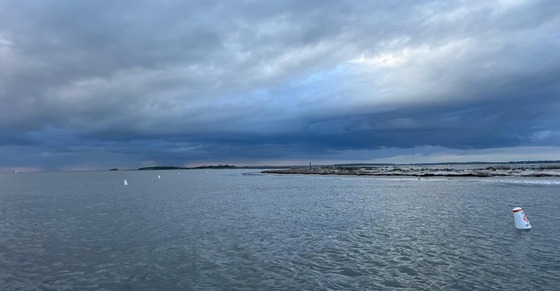 White buoys in gray water near low island against blue-purple clouds