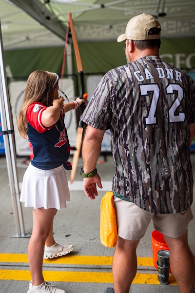 DNR staff in camo jersey instruct girl on archery shooting