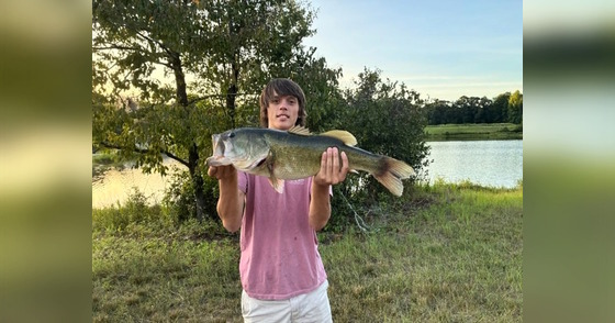 Man in rose-colored T-shirt holding up large bass in both hands
