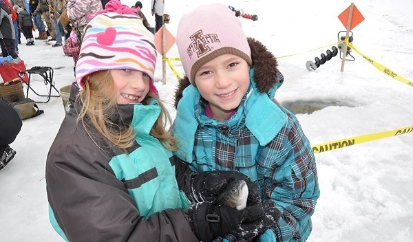 Two girls holding a trout caught through the ice.