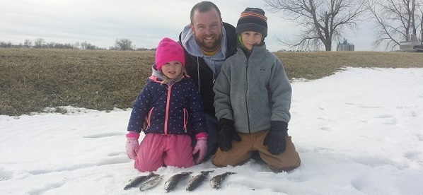 A dad and young daughter and son show off their catch from a community trout stocking event at Lake Petocka.