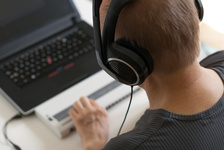 Person with headphones using braille and computer.