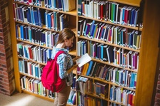 High school student looking at book in library book stacks