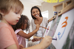 Preschool teacher with two students painting at easels.