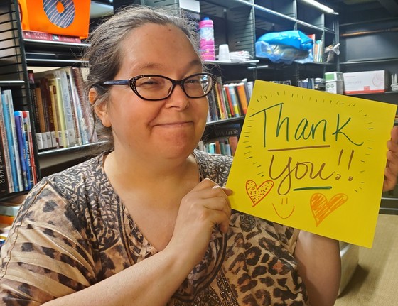 a smiling white woman holds up a sign that says THANK YOU!