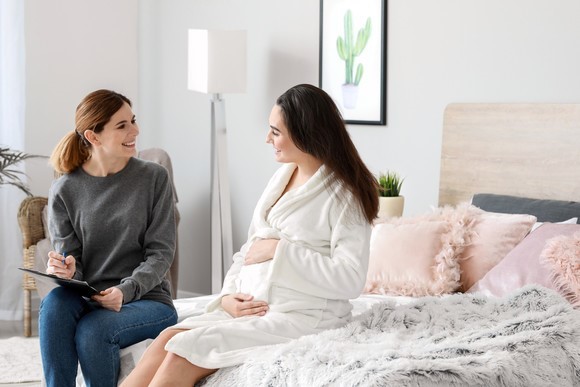 Pregnant Woman Sitting on Bed, Woman with Clipboard sitting next to her