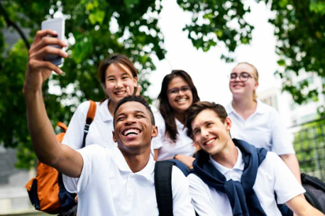 Five teenagers in school outfits taking a selfie on a cell phone