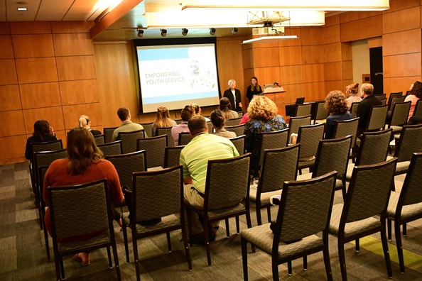 Photo of room filled with conference attendees watching a presentation by two women