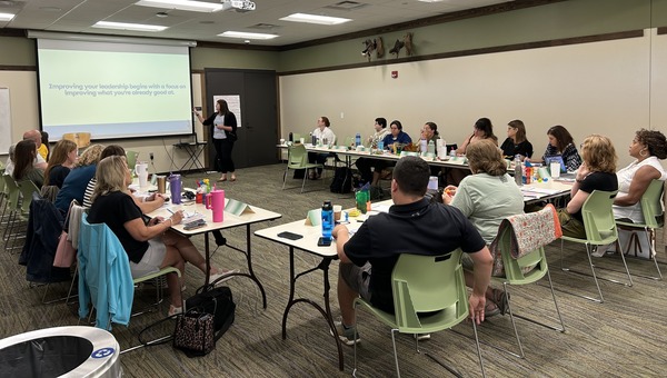 A group of individuals seated at tables in a u shape watching a presentation at the front of the room
