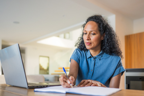 Woman sitting at a computer listening and writing on a notepad